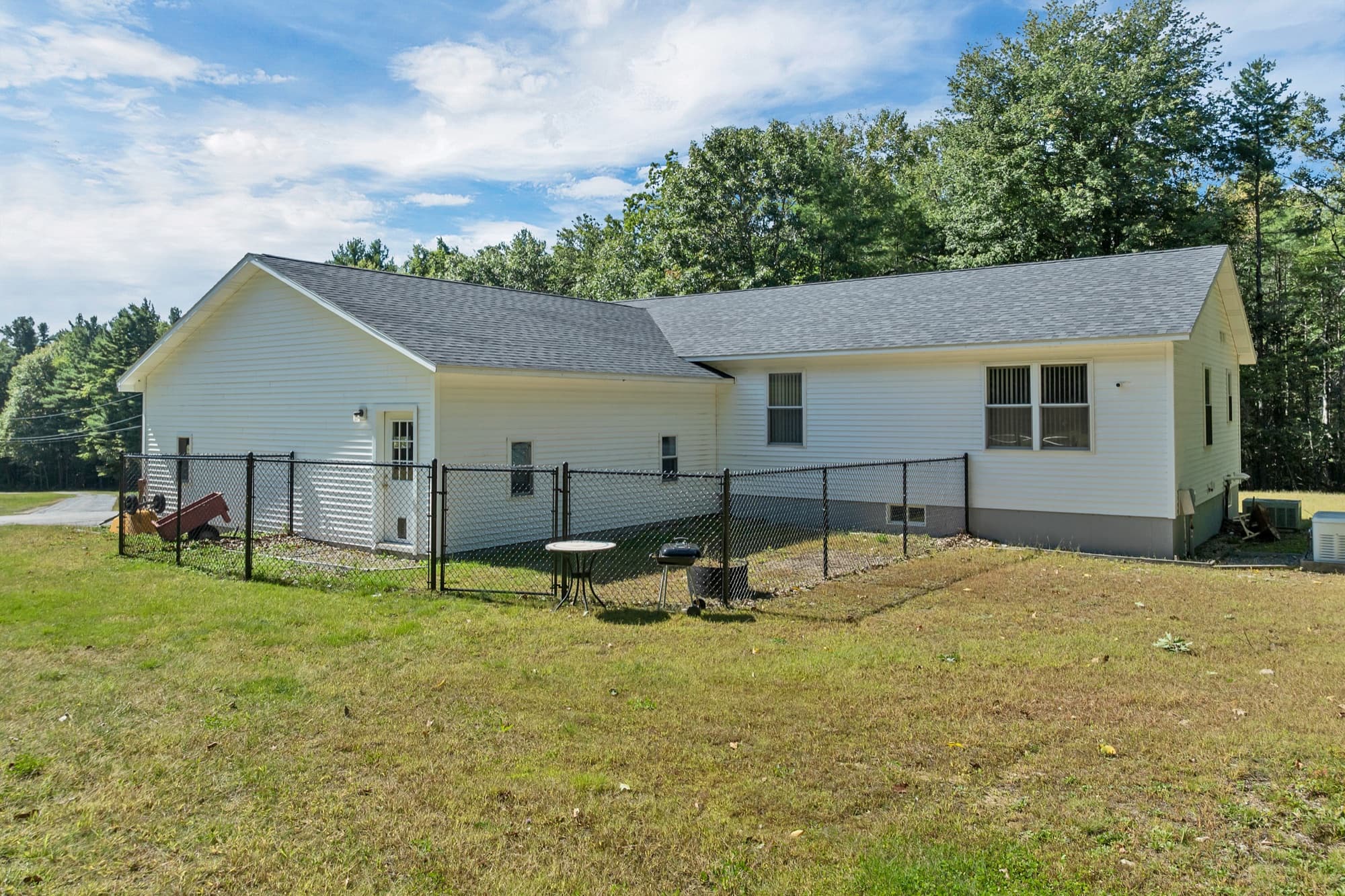 The back of the house with the fenced yard, a patio table, and the woods beyond
