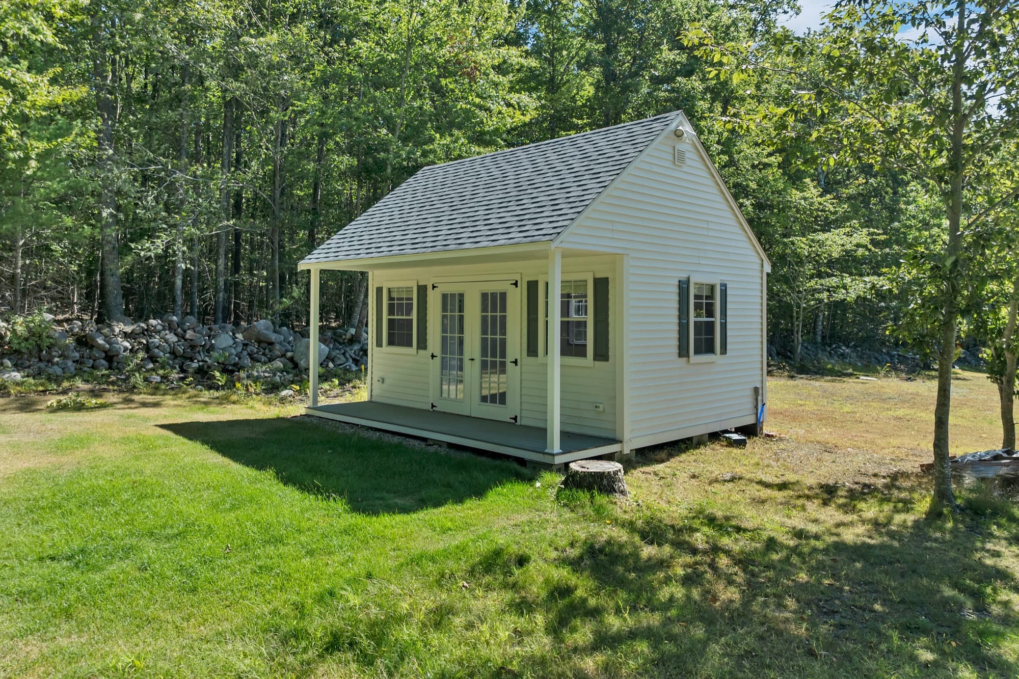 The white studio outbuilding with its covered porch and French doors, at the edge of the woods