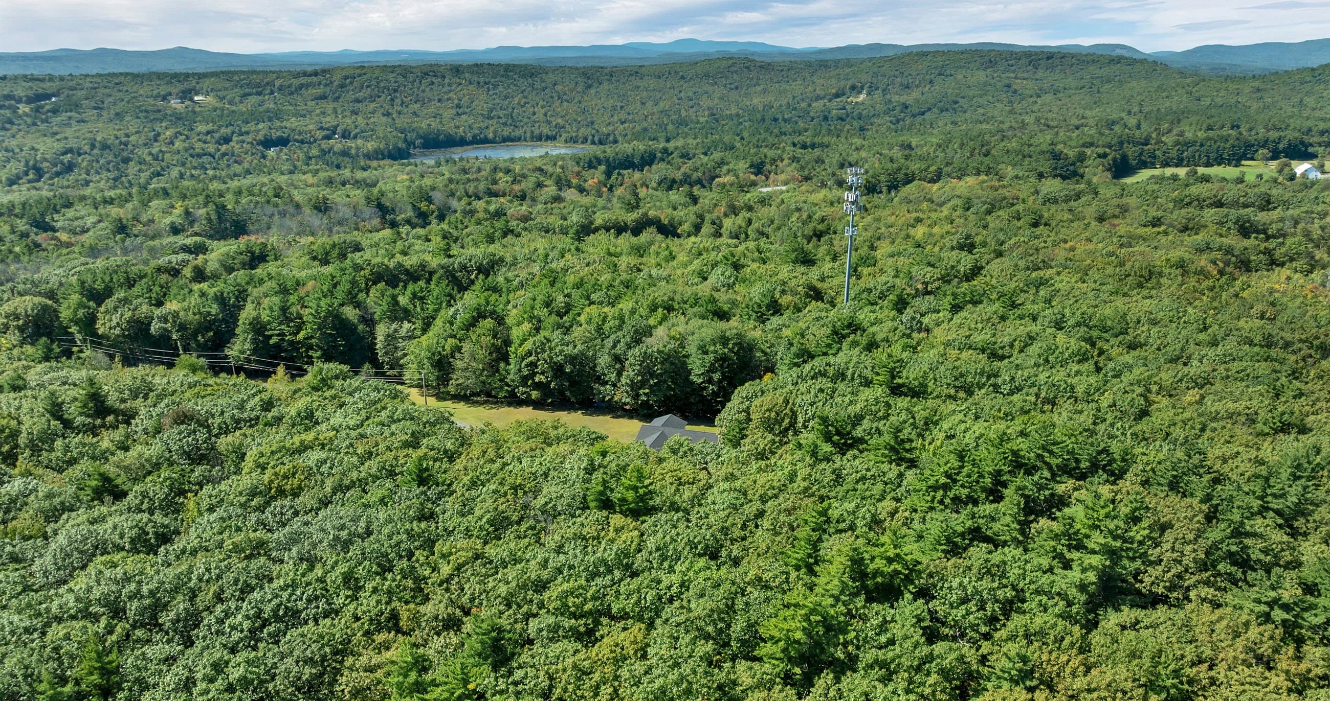 The woods rolling away to the hills on the horizon, with a lake in the distance, from the air above the house